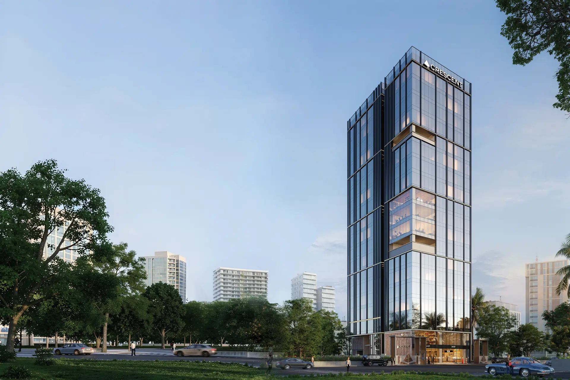The tower seen across the street at daybreak, rising above the trees with the city skyline behind